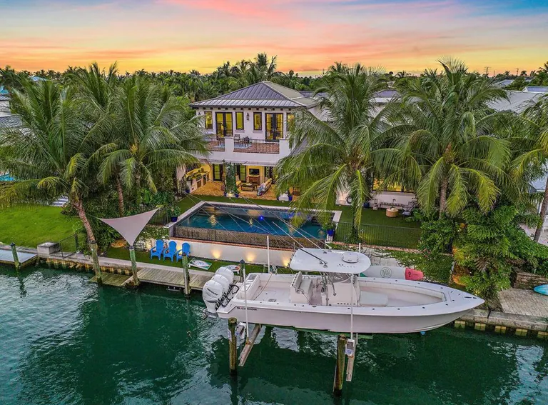 Aerial view of a waterfront home at sunset with a white center console boat on a lift at its private dock